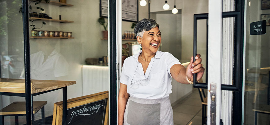 Business owner smiles and opens the front door to the store.